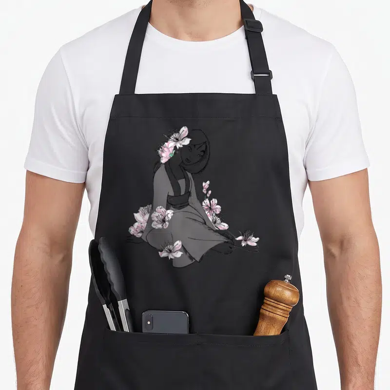 Tablier de cuisine noir avec une illustration esquissée de Mulan assise parmi des fleurs roses aux pétales détaillés.