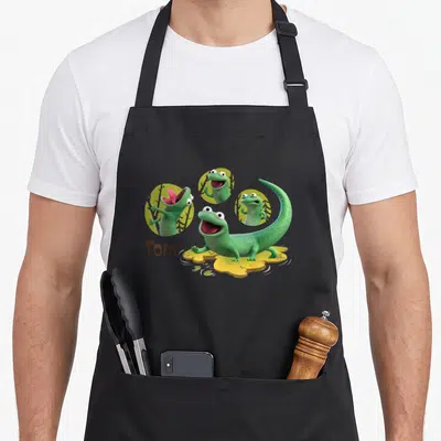 Tablier de cuisine noir avec Tom le lézard vert et trois expressions faciales dans des cercles jaunes.