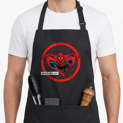 Tablier de cuisine noir avec Spider-Man en position d'atterrissage devant un logo circulaire rouge et l'inscription BRAND NEW DAY.