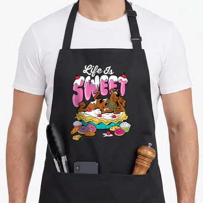 Tablier de cuisine noir avec Scooby-Doo posé sur une tarte et des sucreries sous le texte Life Is Sweet.