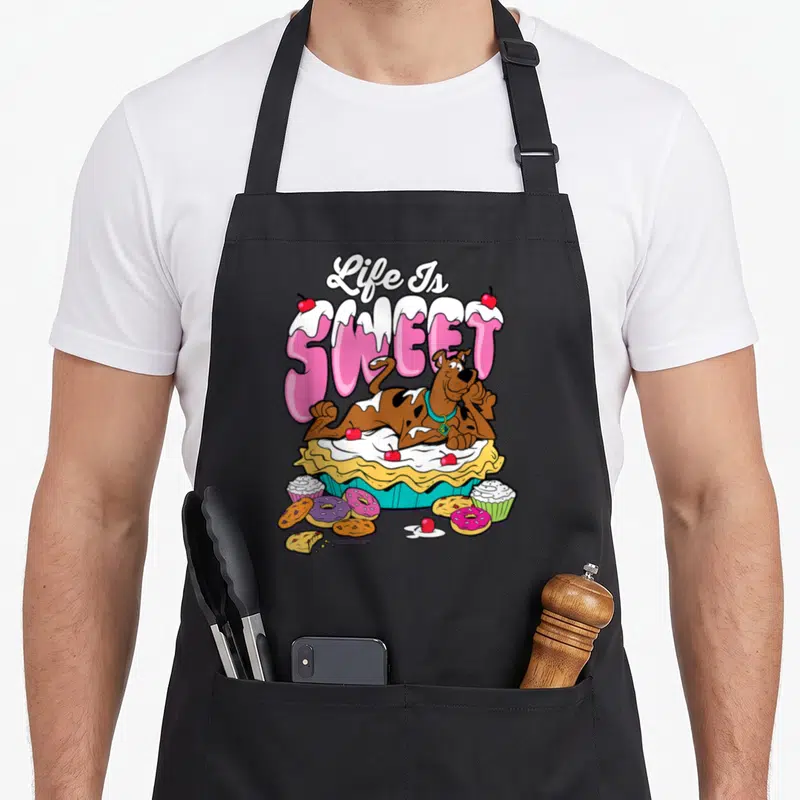 Tablier de cuisine noir avec Scooby-Doo posé sur une tarte et des sucreries sous le texte Life Is Sweet.