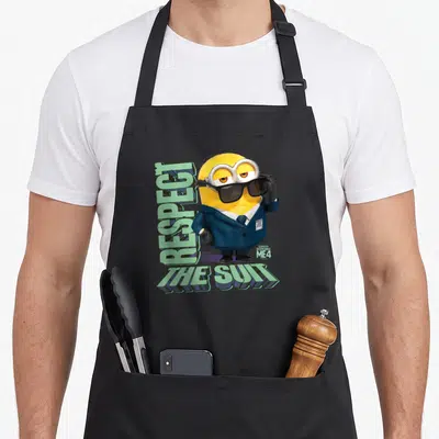 Tablier de cuisine noir avec un Minion en costume bleu portant des lunettes noires et le texte Respect the Suit imprimé en vert.