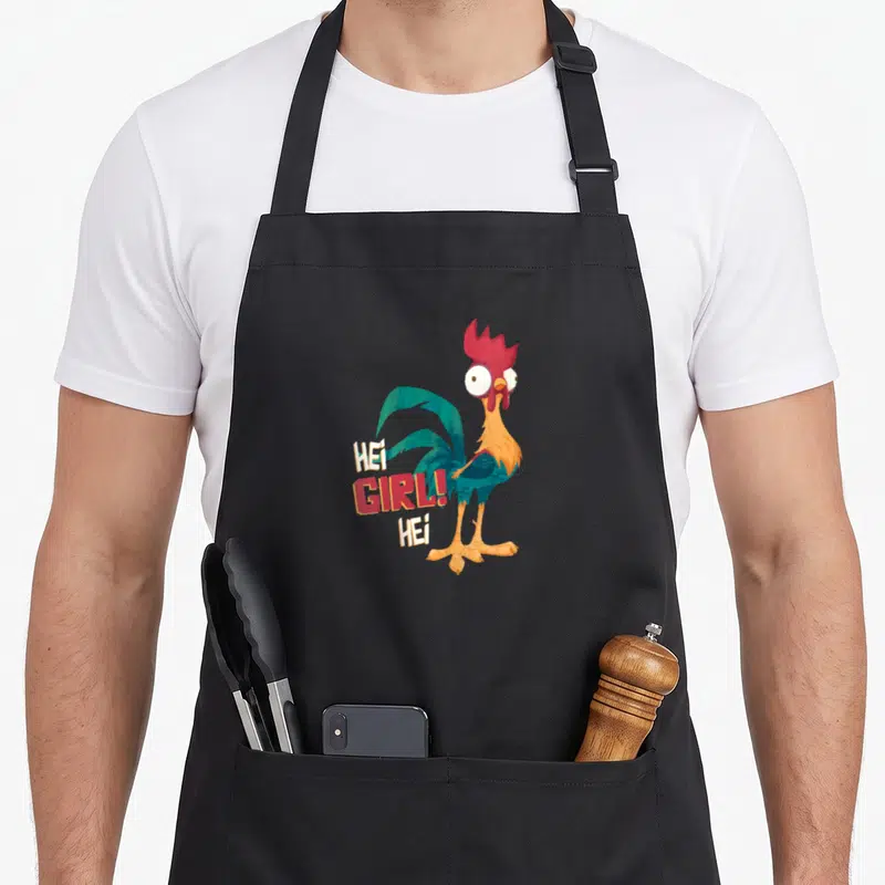 Tablier de cuisine noir avec un coq aux yeux exorbités et l'inscription HEI GIRL HEI en lettres colorées.