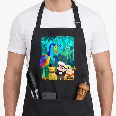 Tablier de cuisine noir avec illustration colorée de Carl Russell, Dug, un kid scout et l'oiseau géant Kevin dans une jungle tropicale.