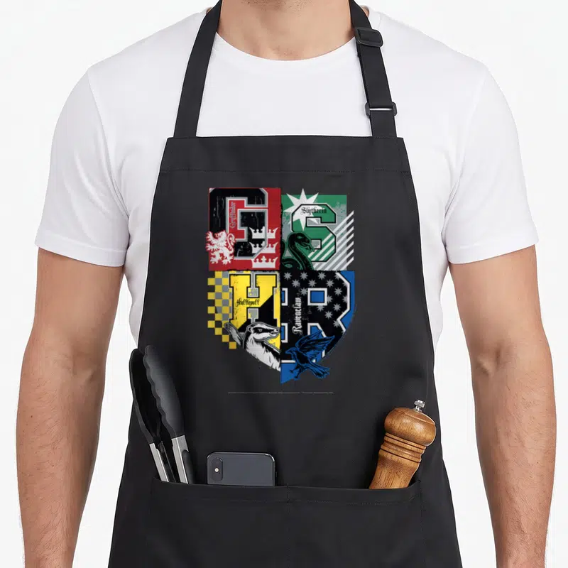 Tablier de cuisine noir avec le logo des quatre maisons d'Hogarts en style Varsity coloré.