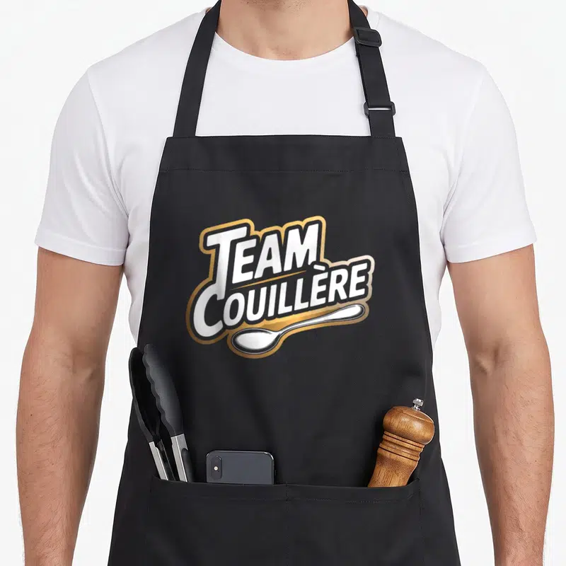 Tablier de cuisine noir avec logo Team Couillère en blanc, gris et or surmontant une cuillère argentée.