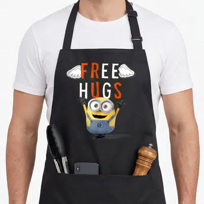 Tablier de cuisine noir avec un Minion jaune aux bras levés et le texte Free Hugs en orange et blanc.
