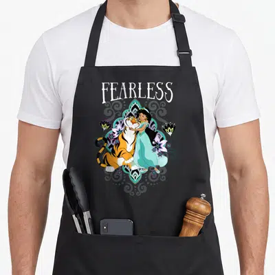 Tablier de cuisine noir avec illustration de Jasmine, Rajah et le mot Fearless entourés de fleurs stylisées.