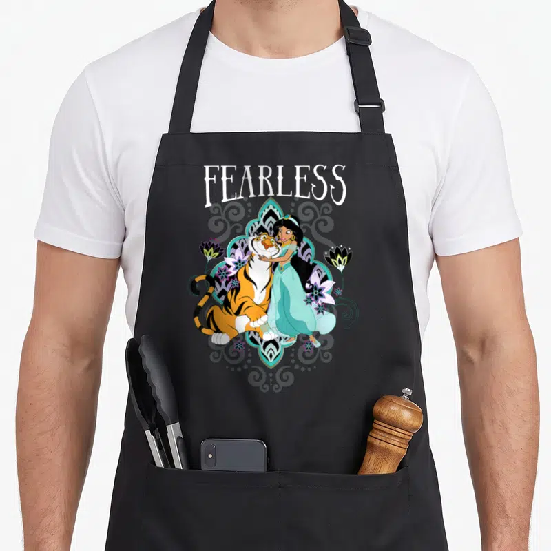 Tablier de cuisine noir avec illustration de Jasmine, Rajah et le mot Fearless entourés de fleurs stylisées.