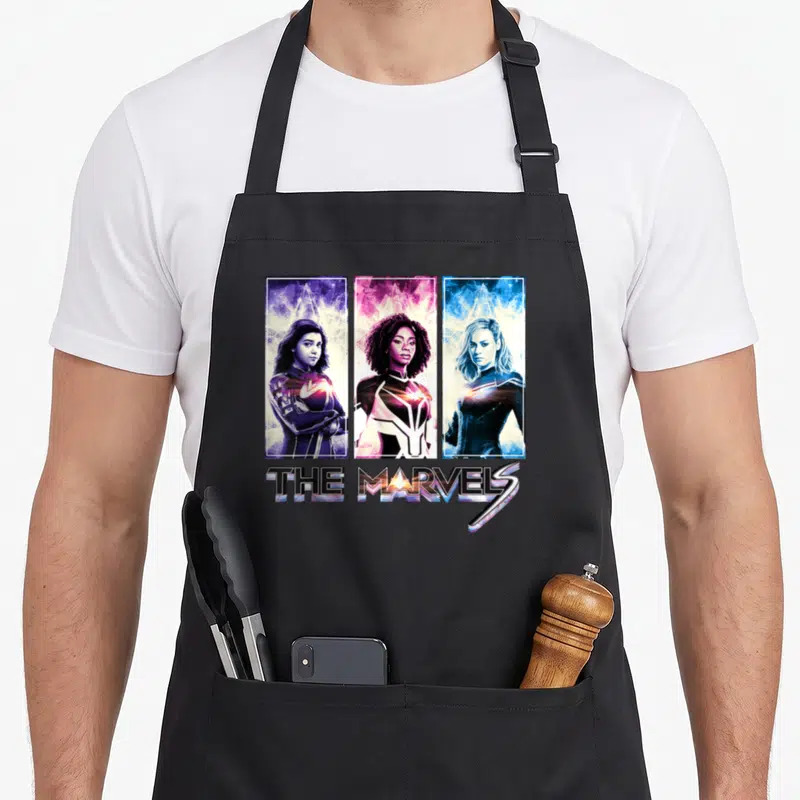 Tablier de cuisine noir avec Miss Marvel, Photon et Captain Marvel en trois panneaux verticaux colorés.