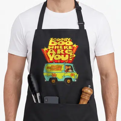 Tablier de cuisine noir avec illustration colorée de la Mystery Machine et du titre Scooby-Doo Where Are You sur fond uni.