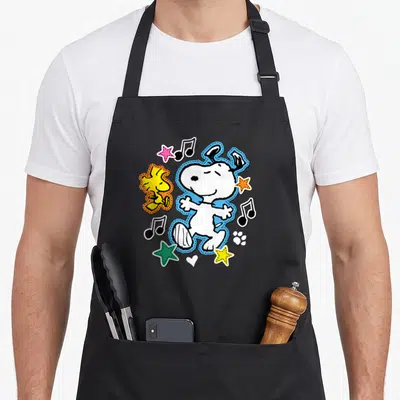 Tablier de cuisine noir avec Snoopy et Woodstock en patchs colorés entourés de notes de musique et d'étoiles.