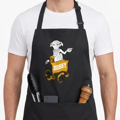 Tablier de cuisine noir avec illustration de Dobby tenant une bannière orange portant le texte DOBBY en lettres blanches.