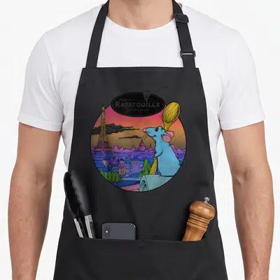 Tablier de cuisine noir avec illustration colorée de Remy surplombant Paris et la Tour Eiffel.