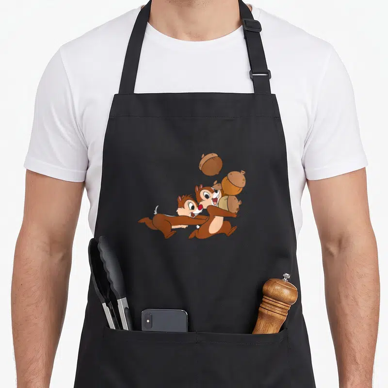 Tablier de cuisine noir avec Chip et Dale courant avec des noix imprimés au centre.