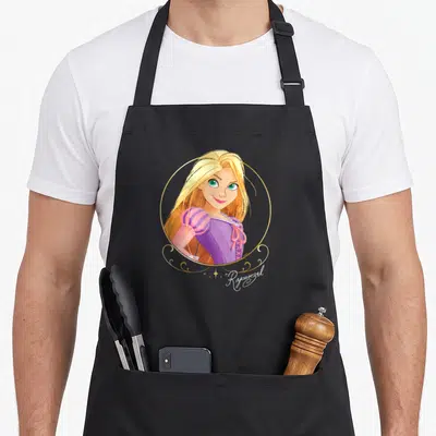 Tablier de cuisine noir avec portrait circulaire de Raiponce et son nom en calligraphie dorée.