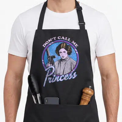 Tablier de cuisine noir avec illustration colorée de LeiaOrgana tenant une arme sous le texte Don't Call Me Princess