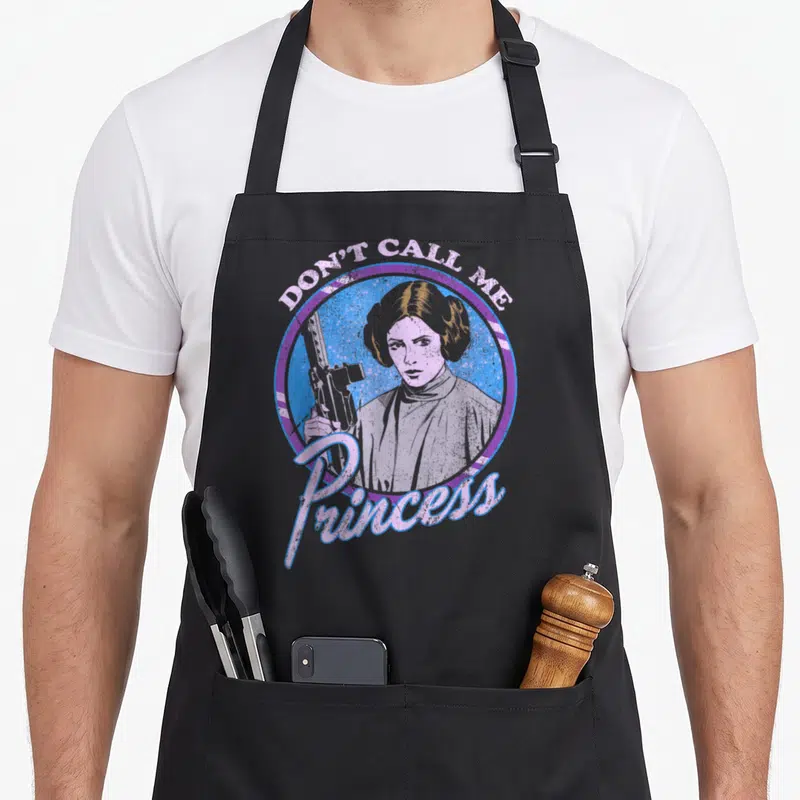 Tablier de cuisine noir avec illustration colorée de LeiaOrgana tenant une arme sous le texte Don't Call Me Princess