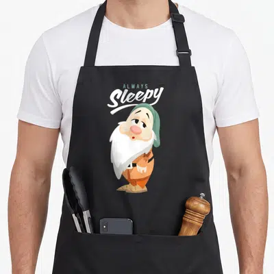 Tablier de cuisine noir avec illustration du nain Always Sleepy coiffé d'un bonnet vert et vêtu de orange.