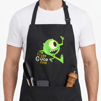 Tablier de cuisine noir avec Mike Wazowski vert sautant et le texte Feels Good Man imprimé en jaune et blanc.