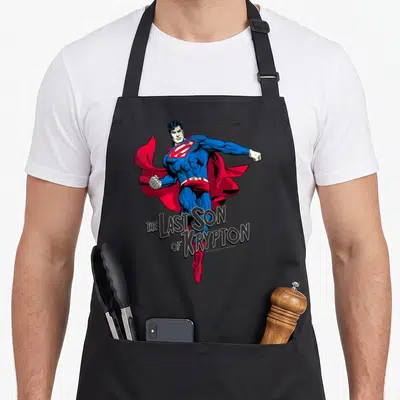 Tablier de cuisine noir avec une illustration de Superman volant et le texte The Last Son of Krypton en dessous.