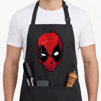 Tablier de cuisine noir avec un grand masque rouge aux yeux blancs et noirs typique d'un personnage de comics.