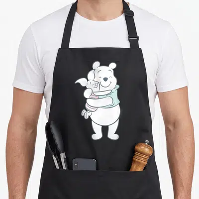 Tablier de cuisine noir avec Winnie l'ourson et Piglet s'enlaçant dans des tons pastel doux.