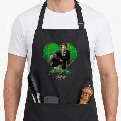 Tablier de cuisine noir avec illustration de Sebastian Sallow dans un cœur vert et le logo Hogwarts Legacy.