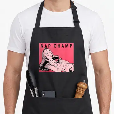 Tablier de cuisine noir avec illustration rose et noire d'Aurora dormant sous le texte Nap Champ.
