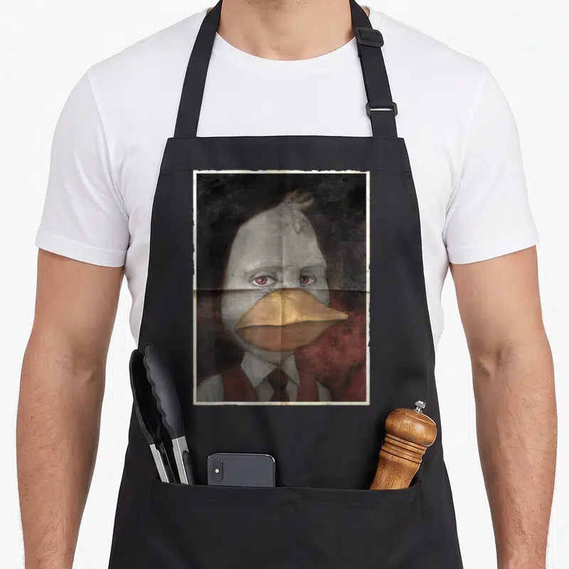 Tablier de cuisine noir avec un portrait peint de Howard the Duck aux yeux rouges et bec doré sur fond sombre.