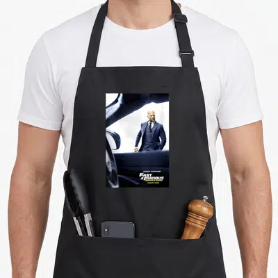 Tablier de cuisine noir avec une illustration de Jason Statham en costume bleu près d'une voiture.