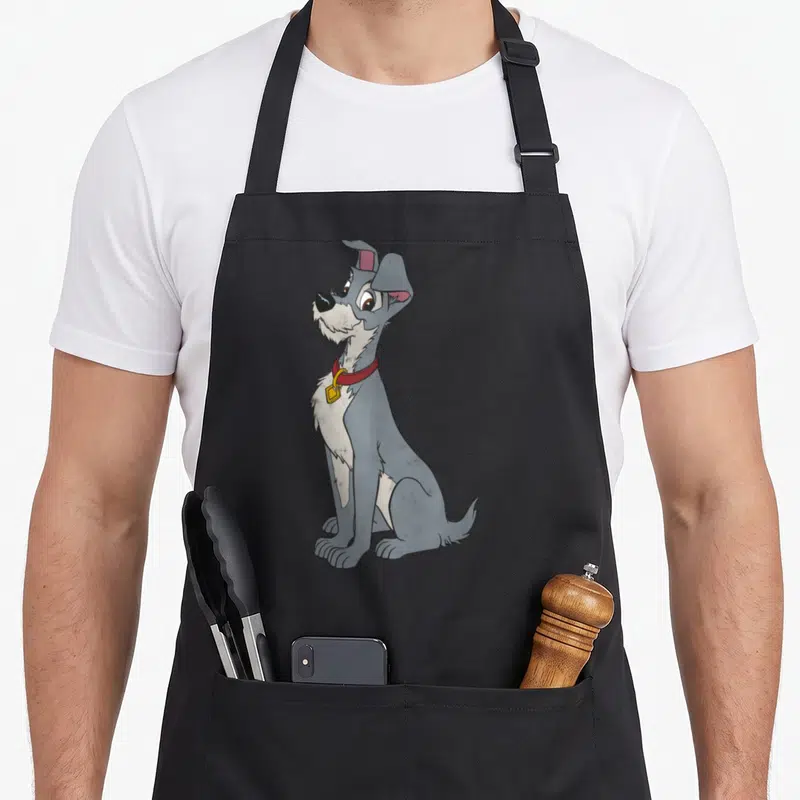 Tablier de cuisine noir avec le portrait assis du chien Le Tramp au collier rouge et à l'expression douce.