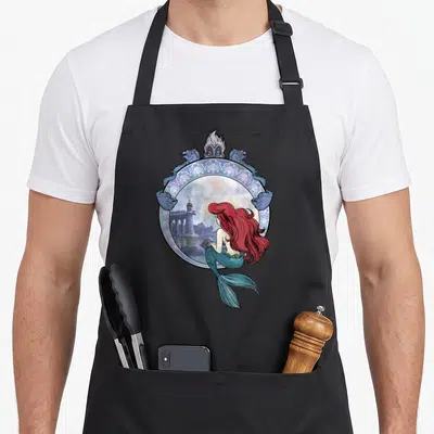 Tablier de cuisine noir avec Ariel regardant une tour dans un cadre orné de sirènes bleues.