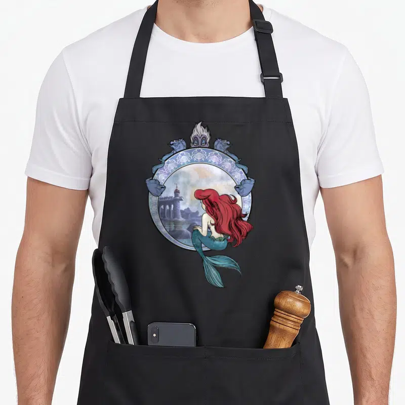 Tablier de cuisine noir avec Ariel regardant une tour dans un cadre orné de sirènes bleues.