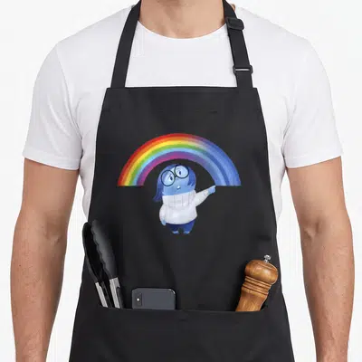 Tablier de cuisine noir avec Triste pointant vers un arc-en-ciel multicolore imprimé au centre.