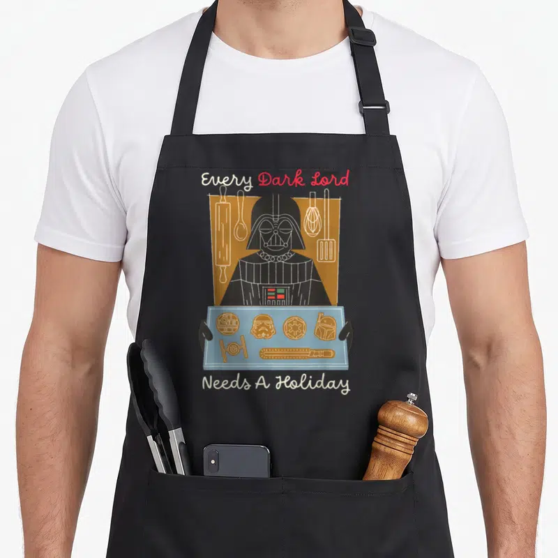 Tablier de cuisine noir avec Darth Vader en biscuit de Noël tenant un plateau de cookies thématiques.
