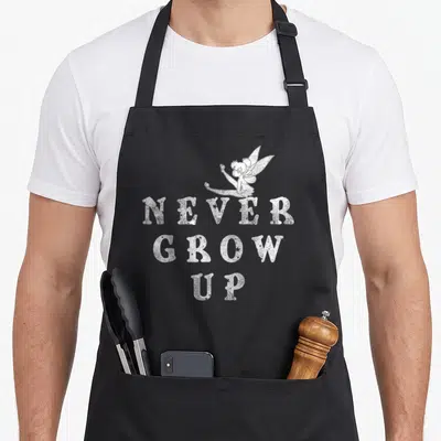 Tablier de cuisine noir avec une illustration blanche de la Fée Clochette et le texte « Never Grow Up » en typographie vintage.