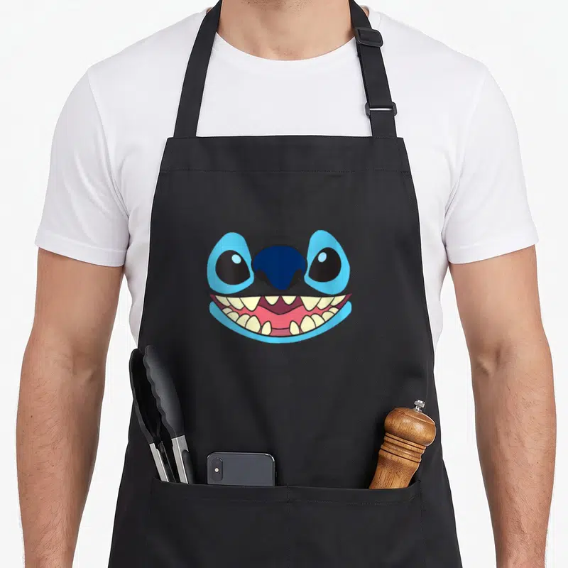 Tablier de cuisine noir avec le visage géant de Stitch affichant un large sourire aux dents pointues.