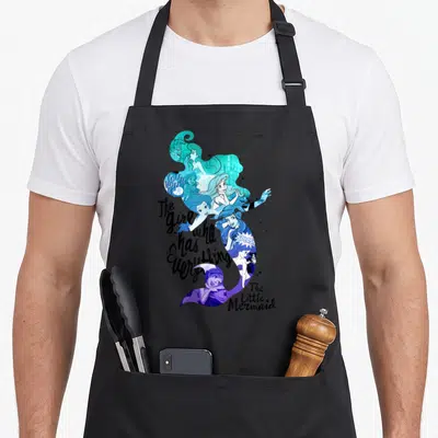 Tablier de cuisine noir avec une grande silhouette colorée de la sirène Ariel contenant plusieurs illustrations et textes.