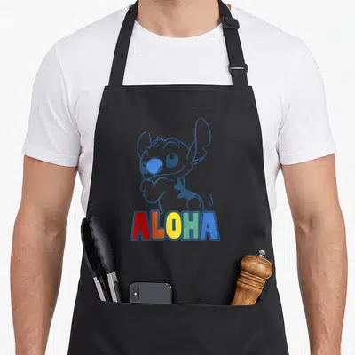 Tablier de cuisine noir avec illustration d'alien bleu et le mot Aloha en lettres colorées.