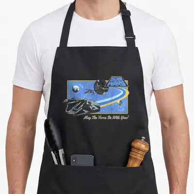 Tablier de cuisine noir avec illustration vintage de la Milennium Falcon et Death Star sur fond bleu.