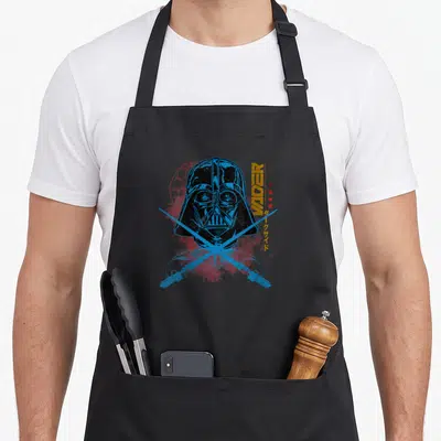 Tablier de cuisine noir avec illustration de Darth Vader et sabres laser bleus croisés sur fond texturé rouge.