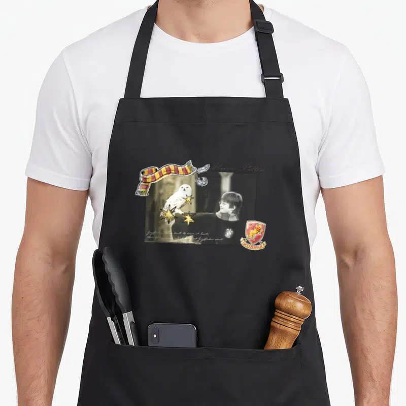 Tablier de cuisine noir avec une composition graphique mêlant Harry Potter, Hedwige, un blason et une écharpe colorée.
