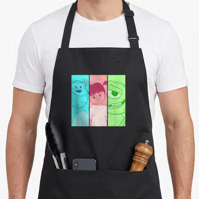 Tablier de cuisine noir avec illustration tripartite de Sulley, Boo et Mike en style dessin animé coloré.