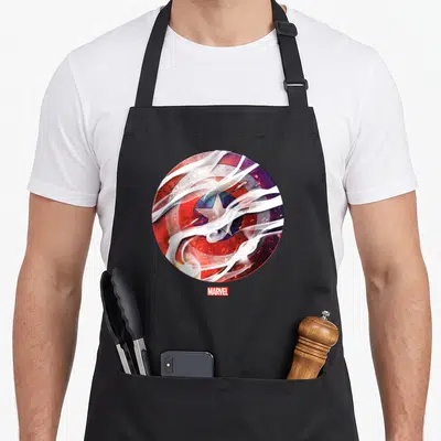 Tablier de cuisine noir avec un bouclier circulaire rouge et bleu traversé par des nuages de fumée blanche et le logo Marvel en bas.