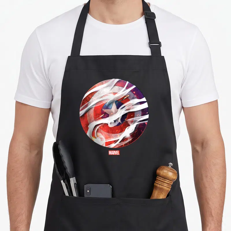 Tablier de cuisine noir avec un bouclier circulaire rouge et bleu traversé par des nuages de fumée blanche et le logo Marvel en bas.