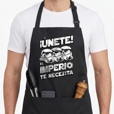 Tablier de cuisine noir avec trois casques de Stormtrooper et le texte ¡ÚNETE. EL IMPERIO TE NECESITA imprimé en blanc.