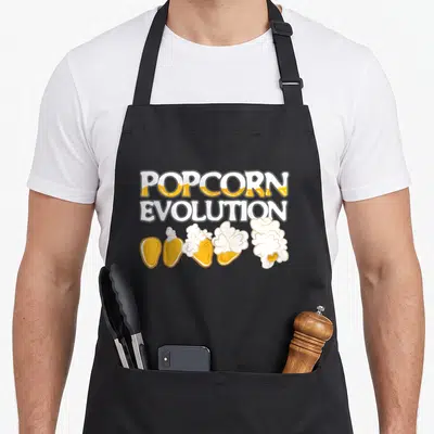 Tablier de cuisine noir avec l'inscription POPCORN EVOLUTION et une illustration de grains de maís transformés en popcorn blanc et jaune.