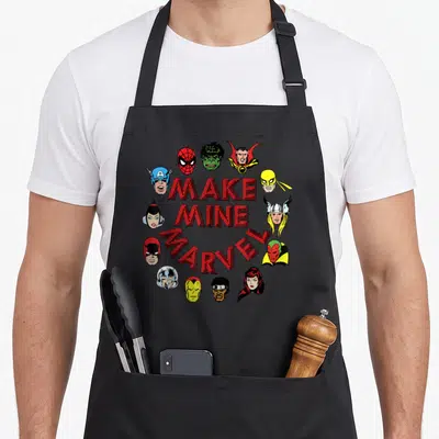 Tablier de cuisine noir avec un cercle de têtes de super-héros colorées et le texte Make Mine Marvel en lettres rouges au centre.