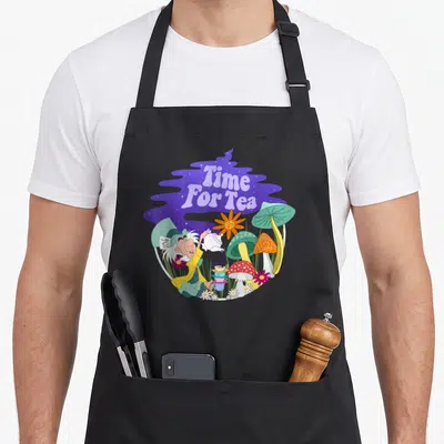 Tablier de cuisine noir avec illustration colorée du Mad Hatter versant le thé entre des champignons et des fleurs dans un décor violet.